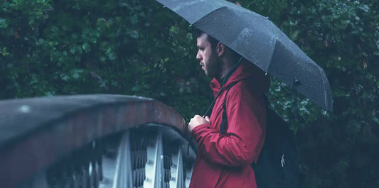Mann mit Schrim im Regen uf einer Brücke in der Dämmerung