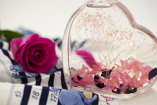 Herz aus Pleixglas mit Wasser und blüten auf einem Tisch mit einer Rose